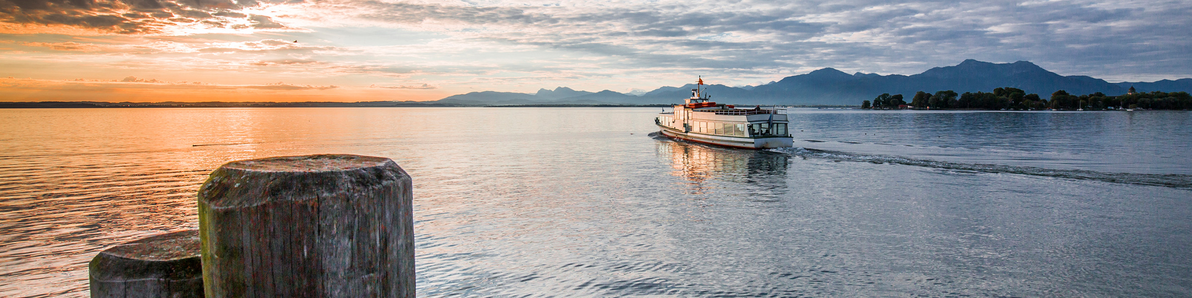 Sonnenuntergang über einem ruhigen See mit Boot im Vordergrund.