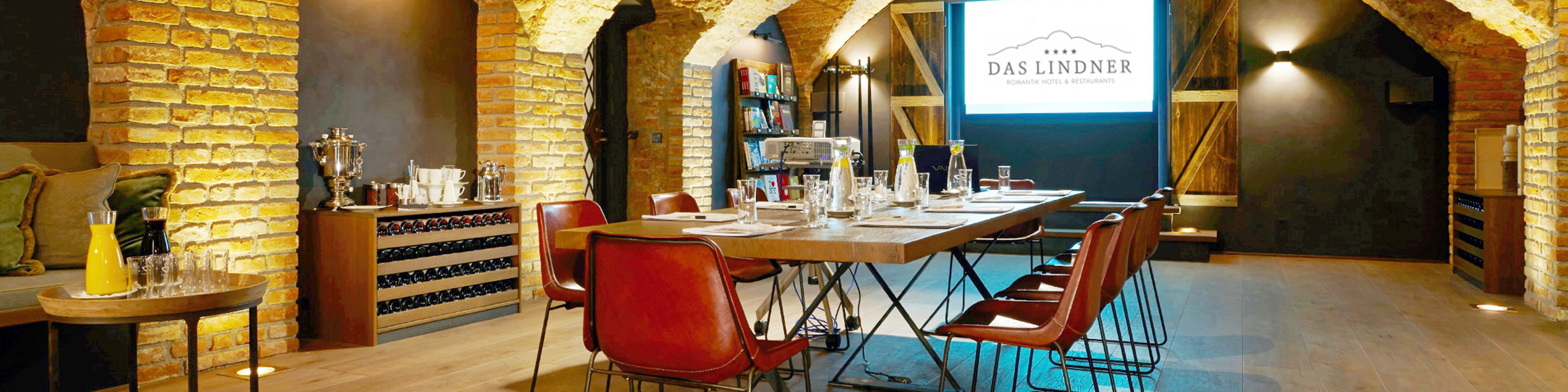 Gedeckter Tisch mit roten Stühlen und einer Leinwand in rustikalem, warmen Weinkeller.
