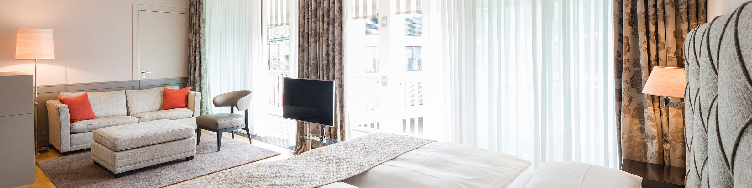 Helles Hotelzimmer mit großen Fenstern und weißem Bett.