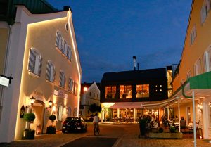Beleuchtetes Hotelgebäude am Abend mit Gästen vor dem Eingang.