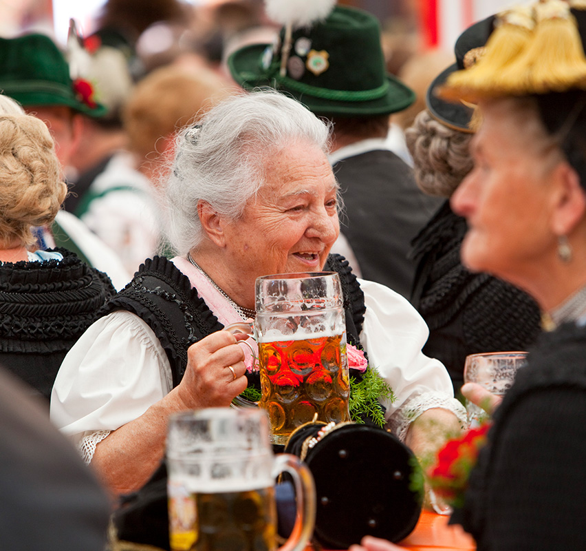 Eine ältere Dame in Tracht beim Biertrinken auf einem Volksfest.
