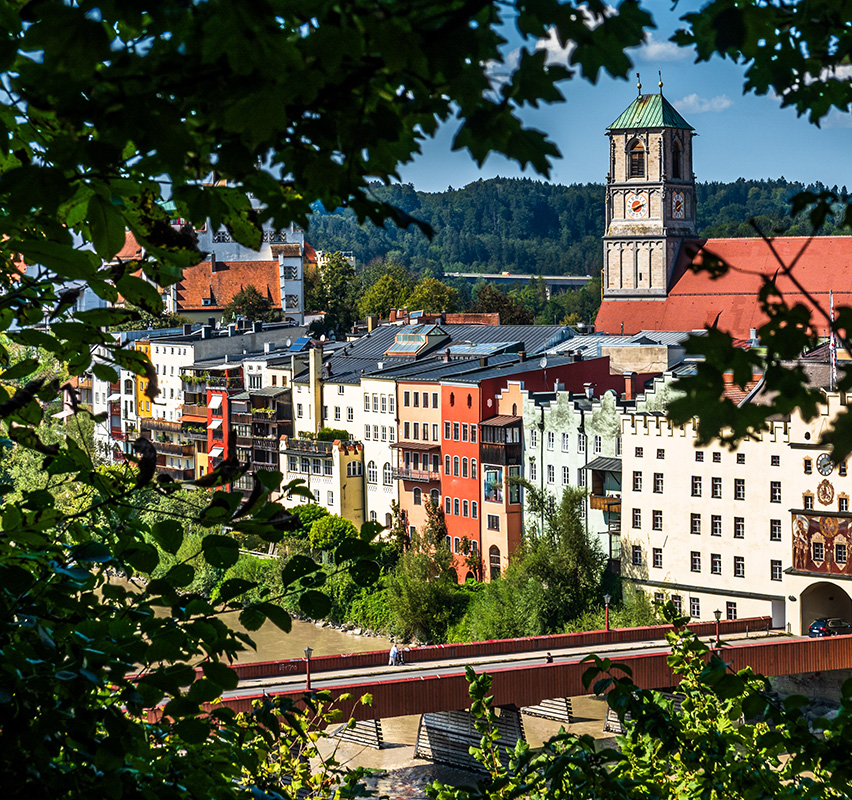 Farbenfrohe Häuserfassaden in Wasserburg vor Bergkulisse.