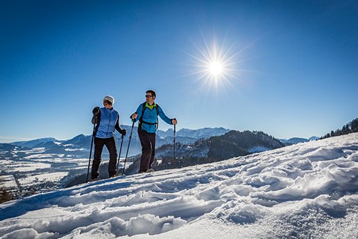 Zwei Personen wandern auf einem verschneiten Berggipfel bei Sonnenschein.