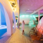Therme Bad Aibling, Frau im Bademantel blickt auf Thermalbäder unter Kuppeln.