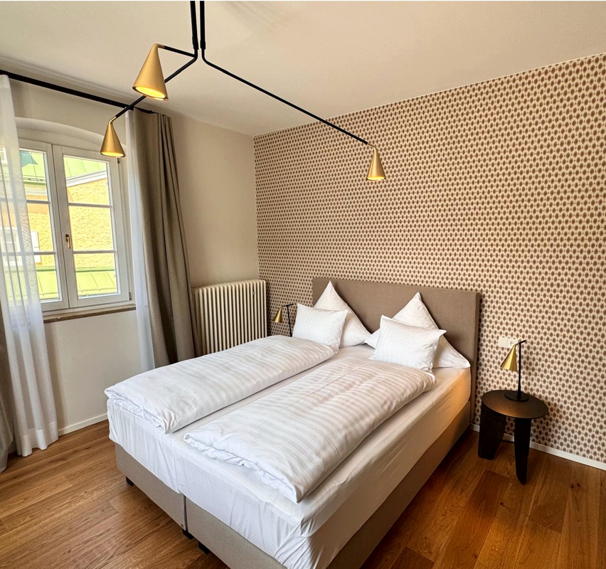 Gemütliches Komfortzimmer im Hotel Das Lindner in Bad Aibling mit Doppelbett, stilvoller Akzentwand, großen Fenstern, eleganten Nachttischen und hochwertiger, moderner Ausstattung.