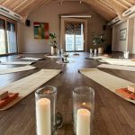Yogamatten und Kerzen in besinnlicher Stimmung im Kreis angeordnet in Raum mit Holzboden.