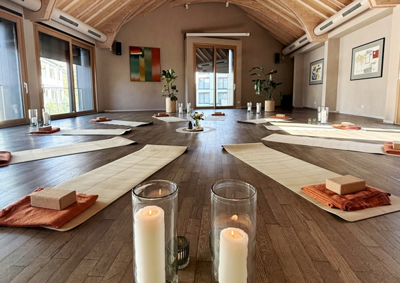 Yogamatten und Kerzen in besinnlicher Stimmung im Kreis angeordnet in Raum mit Holzboden.
