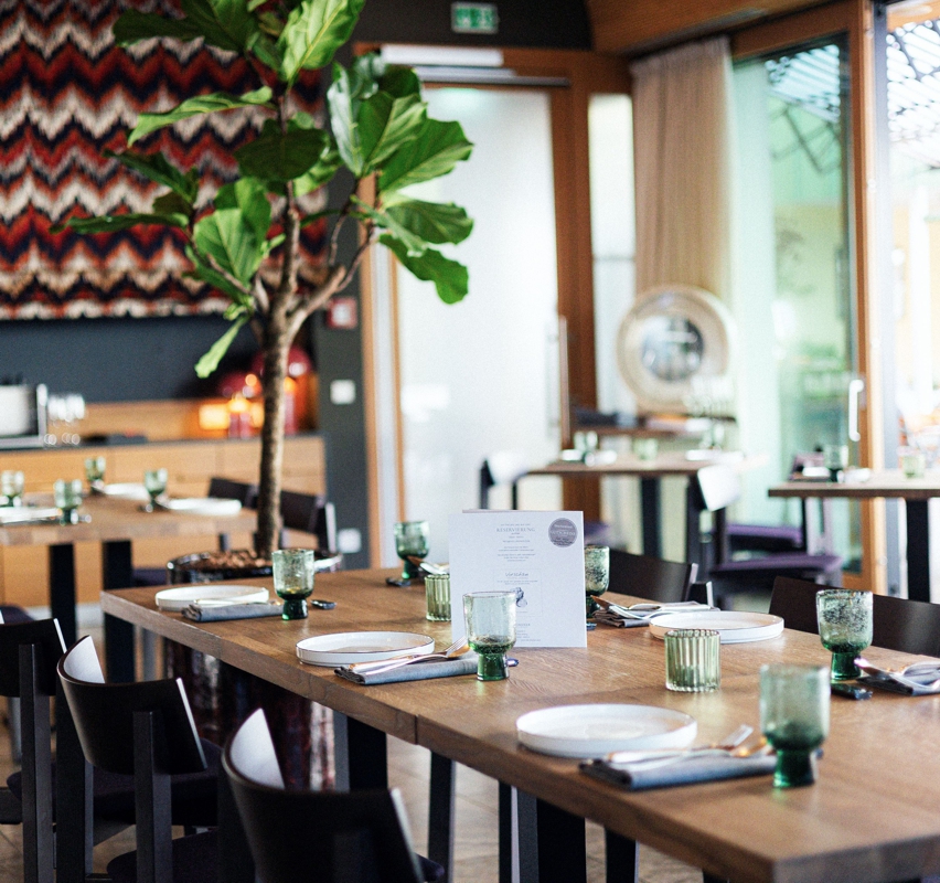 HotelLindner_Waage01_800 Gedeckte Holztische im Restaurant Lindners Waage mit modernen Tellern und Gläsern.